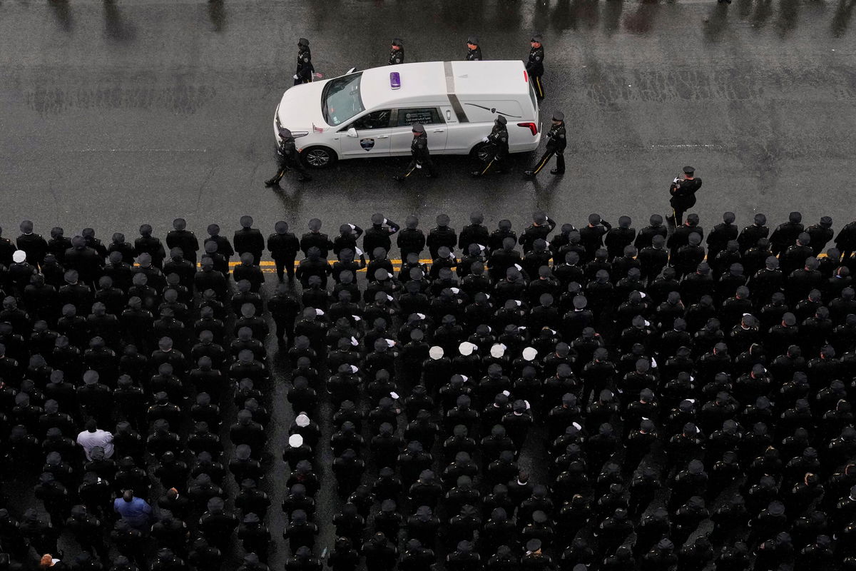 <i>Yuki Iwamura/AP via CNN Newsource</i><br/>Officers flank each side of the white hearse carrying Islam's remains as it drives down White Plains Road after the funeral service on Thursday.