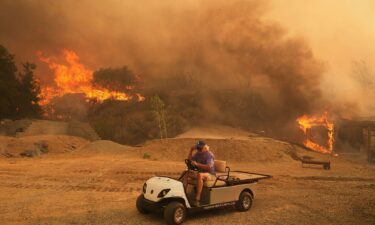 A resident rides a golf cart as he exits his property while the Canyon Fire burns on Thursday in Halsey Canyon